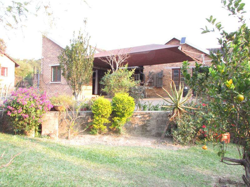 Rear view of a face brick house featuring a large shade sail over the patio area and established garden landscaping.