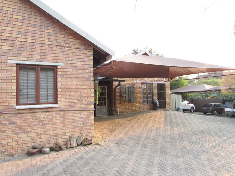 Front exterior view of the property featuring a face brick facade, paved driveway, and a large shade sail carport providing covered parking.