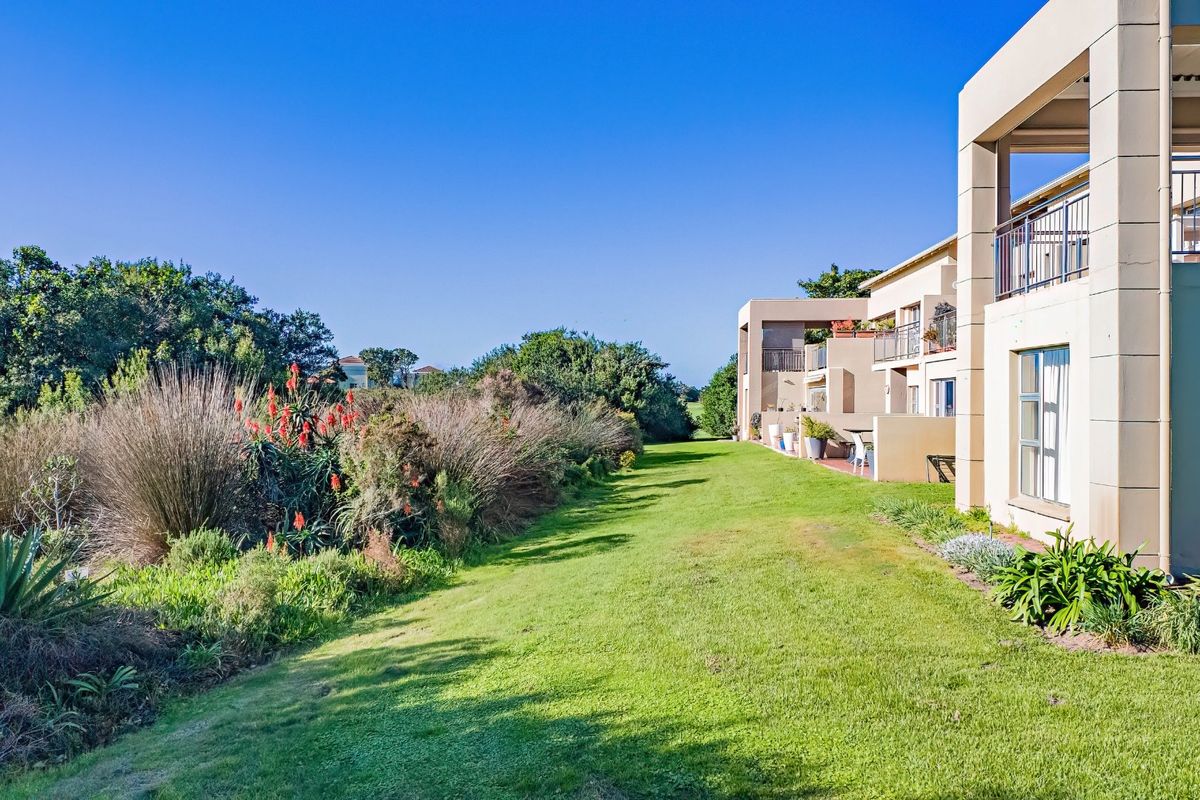 Rear view of the apartment complex featuring private balconies, paved patio areas, and a well-maintained communal lawn with established garden landscaping.