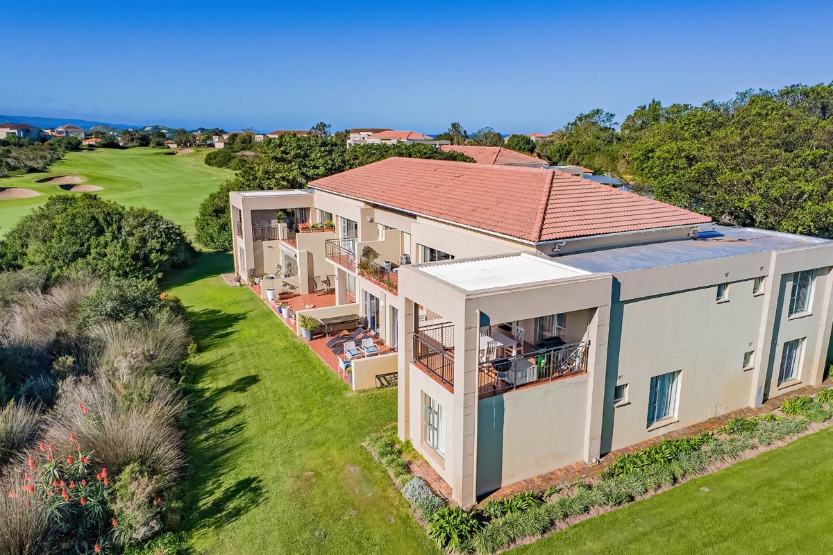Aerial view of an apartment complex featuring tiled roofs, private balconies, and a well-maintained garden overlooking a golf course.