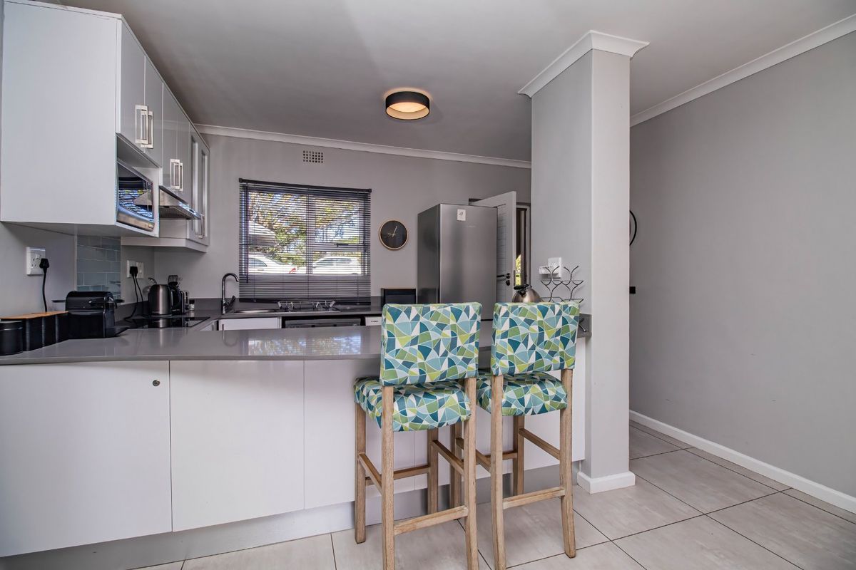 Modern kitchen featuring sleek white cabinetry, stone countertops, a breakfast bar, and integrated appliances, finished with neutral tiled flooring and clean lines.