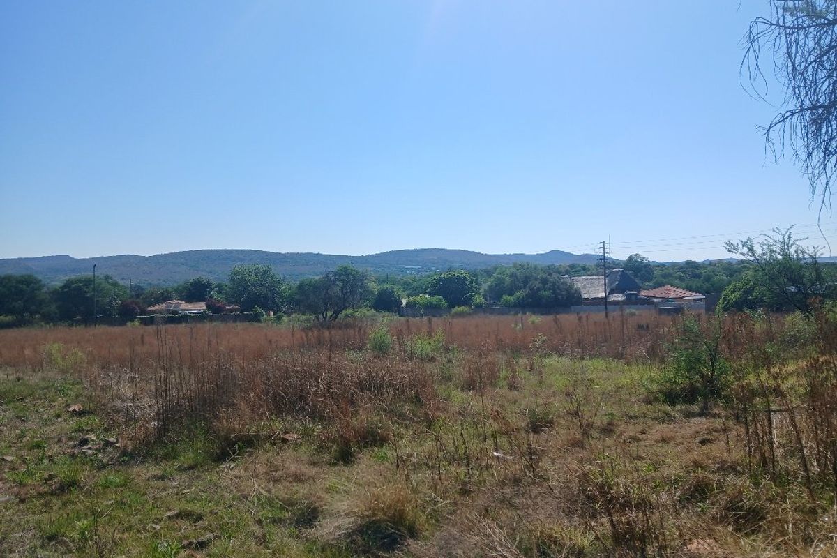A view of an undeveloped residential plot featuring natural vegetation with distant hills and surrounding neighborhood structures in the background.