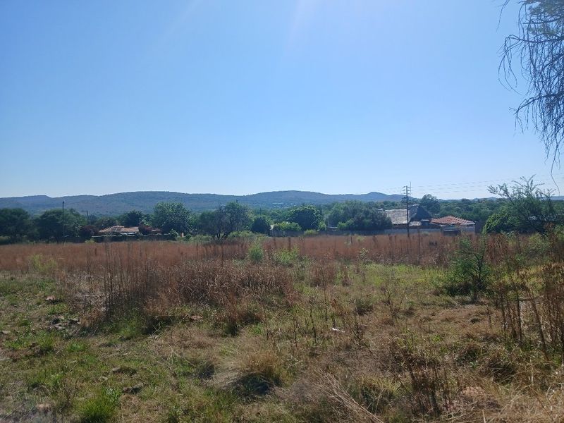 A view of an undeveloped residential plot featuring natural vegetation with distant hills and surrounding neighborhood structures in the background.