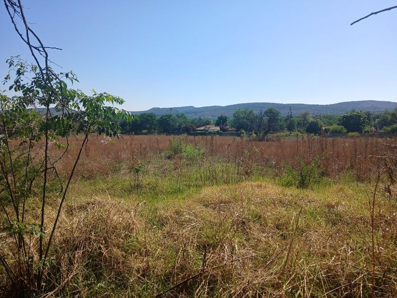A view of the vacant residential land featuring dry grass and vegetation with distant hills and trees in the background.