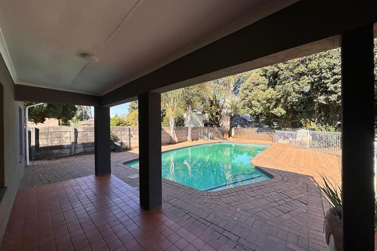 A covered patio area overlooking a swimming pool with brick paving and perimeter boundary walls.