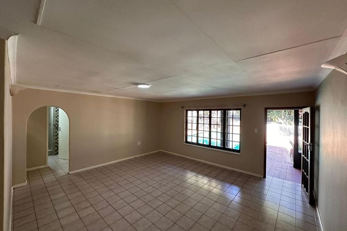 Spacious, empty living area featuring neutral tiled flooring, an arched entryway, and direct access to the outdoor patio area.