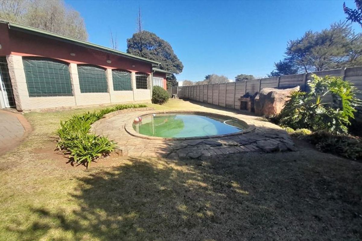 Rear garden area featuring a swimming pool, stone paving, and a built-in braai, enclosed by a precast concrete boundary wall.