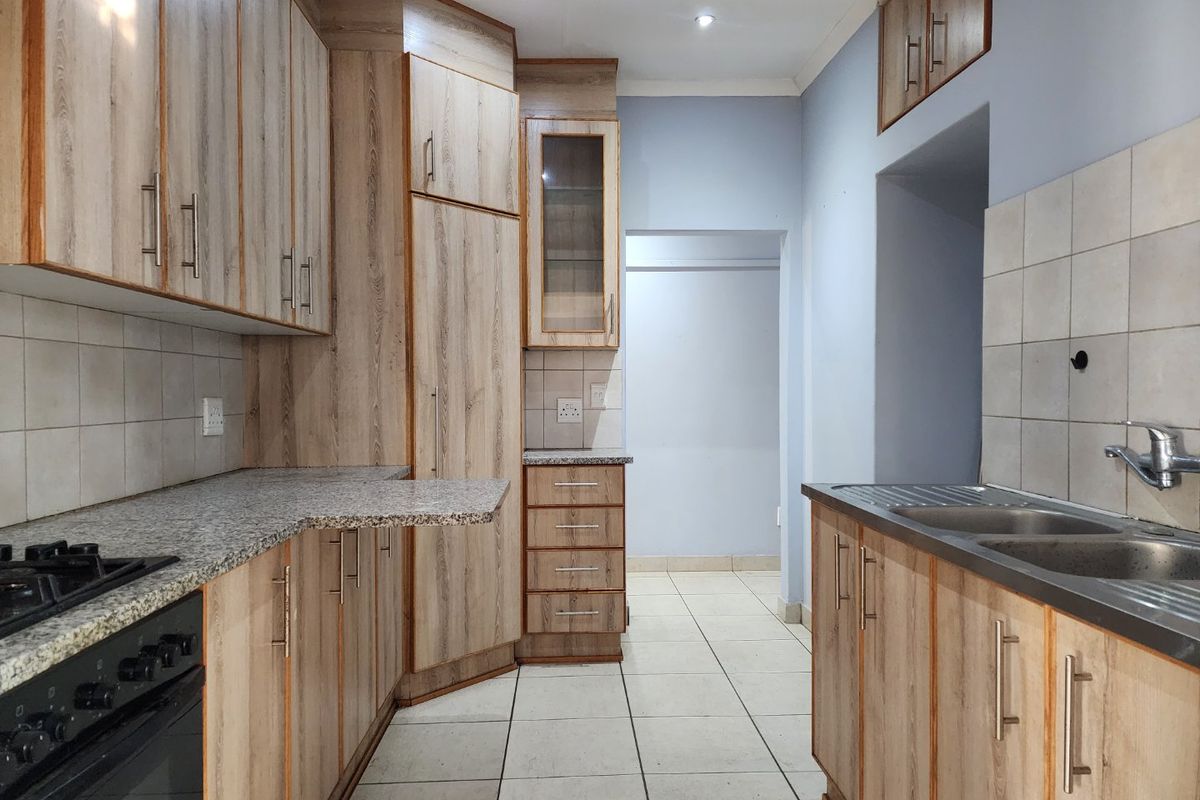 A clean, functional kitchen featuring wood-look cabinetry, granite countertops, a double sink, and built-in cooking appliances with neutral tiled flooring.