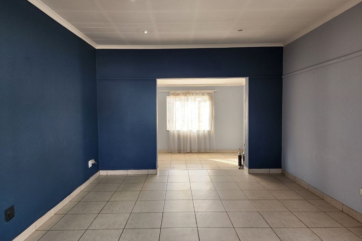 An empty, open-plan living area featuring tiled flooring, recessed ceiling lights, and contrasting blue and light-toned walls, leading into an adjacent room.