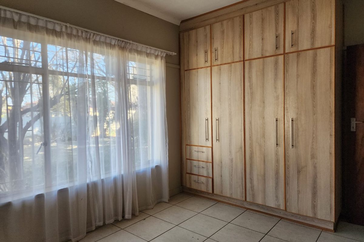 A bright, empty bedroom featuring neutral tiled flooring and extensive floor-to-ceiling built-in wooden cupboards.