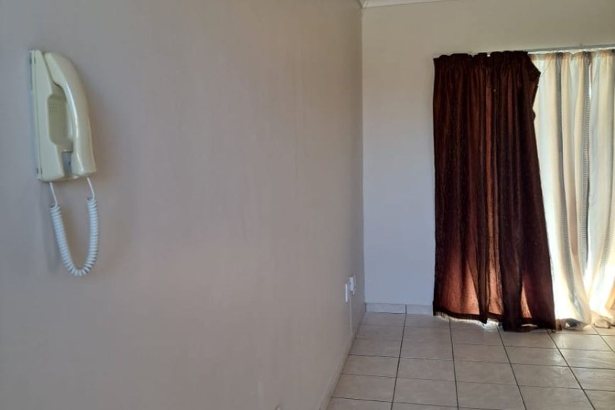 An empty living area featuring ceramic floor tiles, coved ceiling cornices, and a wall-mounted intercom system, ready for personalization.