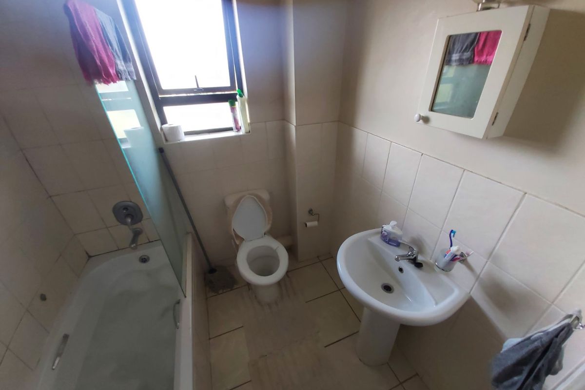 A compact bathroom featuring a pedestal basin, toilet, and a bathtub with a glass shower screen, finished with neutral wall and floor tiling.