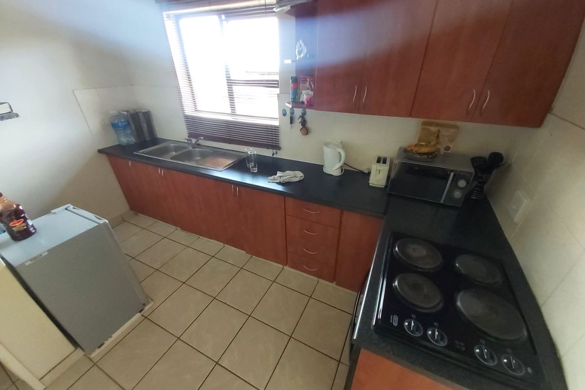 A functional kitchen featuring laminate cabinetry, dark countertops, a double bowl sink, and an integrated electric hob with tiled flooring.