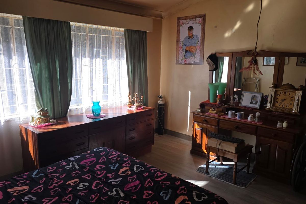 A bedroom featuring laminate flooring and a large window with security bars, offering natural light and a functional layout.