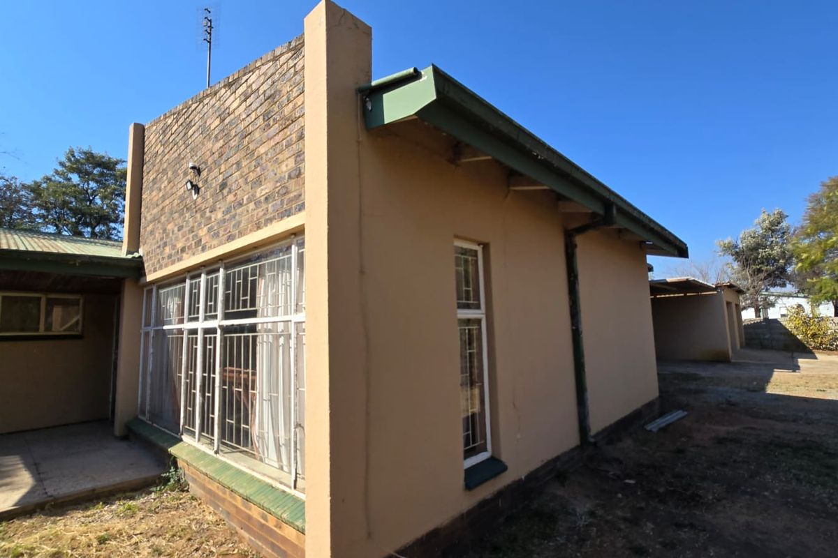 Rear exterior view of the house featuring brick and plaster finishes, metal roofing, and security bars on the windows.