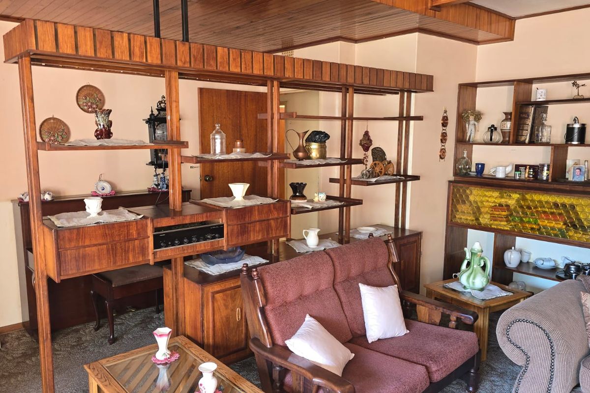 A living room featuring a prominent built-in timber shelving unit and a timber-paneled ceiling, offering a dated aesthetic ready for modernization.