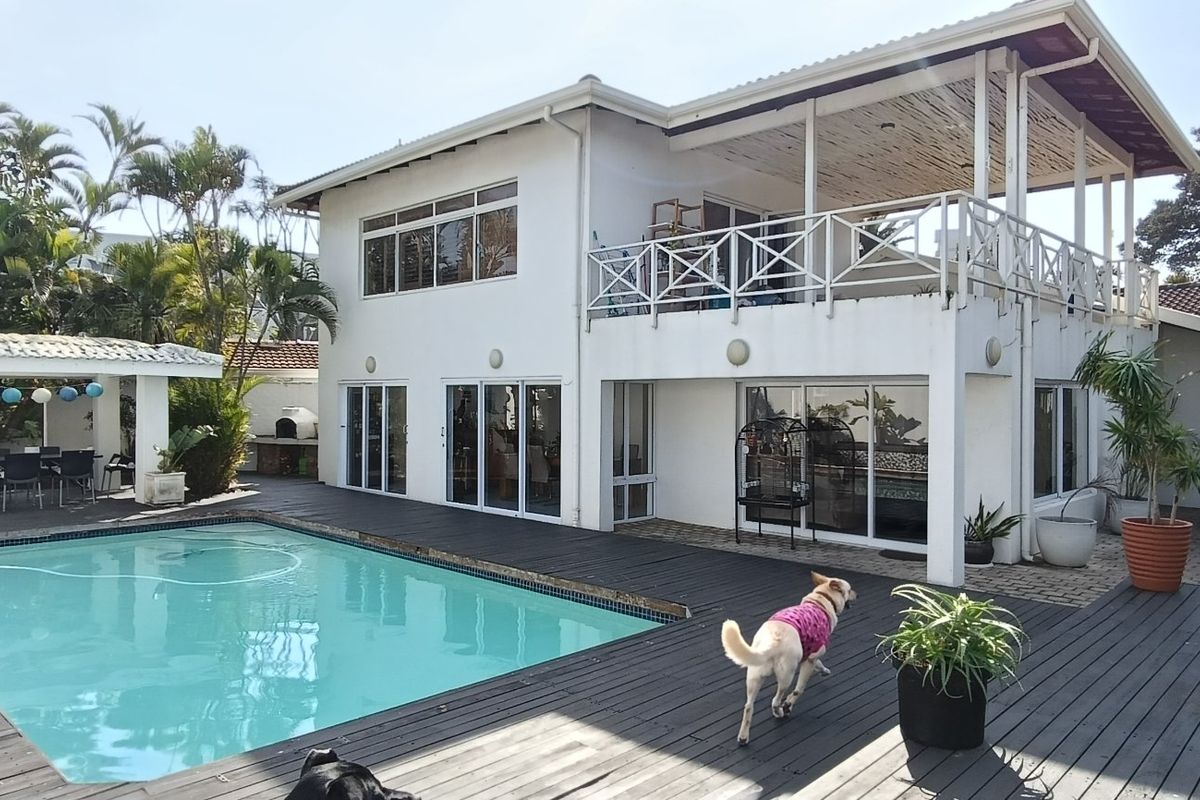 Rear exterior view featuring a swimming pool, extensive timber decking, a covered patio area, and an upper-level balcony with white railings.