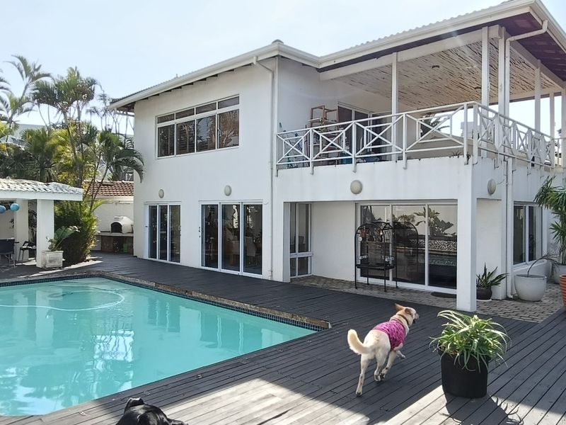 Rear exterior view featuring a swimming pool, extensive timber decking, a covered patio area, and an upper-level balcony with white railings.