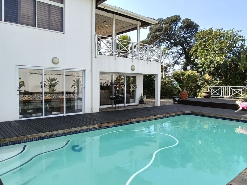 Outdoor pool area featuring extensive timber decking, a raised balcony, and direct access to the home through large sliding glass doors.