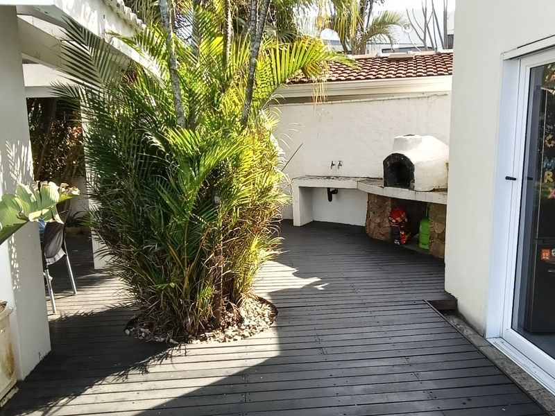 Covered outdoor patio featuring timber decking, a built-in braai, and a prep counter, providing a functional space for outdoor entertaining.