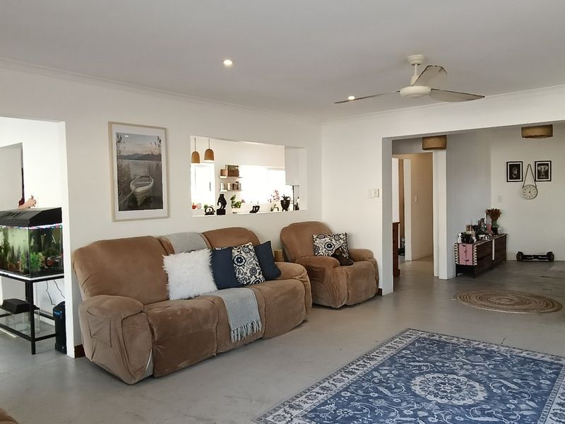 Spacious open-plan living area featuring neutral walls, recessed downlighting, a ceiling fan, and a convenient pass-through window connecting to the kitchen.