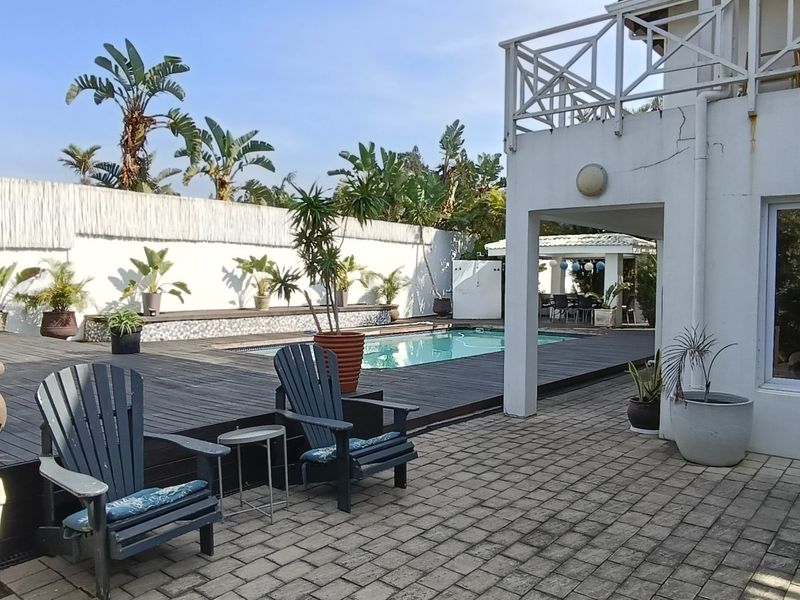 Outdoor pool area featuring timber decking, paved patio space, and a balcony overlooking the swimming pool and garden.
