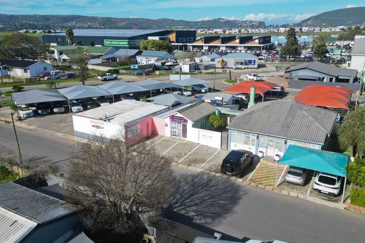 Aerial view of a commercial property complex featuring multiple storefronts, paved parking areas, and extensive shade cloth carports in a suburban setting.