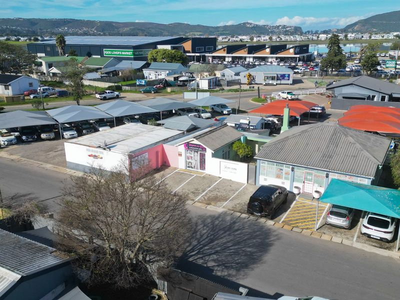 Aerial view of a commercial property complex featuring multiple storefronts, paved parking areas, and extensive shade cloth carports in a suburban setting.