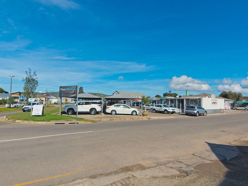 Street-level view of a commercial property featuring a paved display area, shade cloth carports, and prominent business signage.