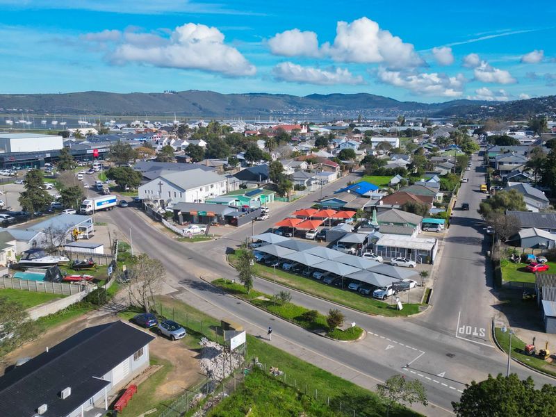 An aerial view of a commercial area featuring parking facilities, road networks, and surrounding urban development with a coastal backdrop.