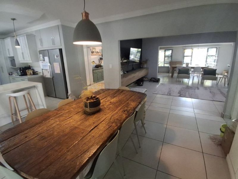Spacious open-plan living area featuring a modern kitchen with island, dining space, and a connected lounge with built-in media cabinetry and tiled flooring.
