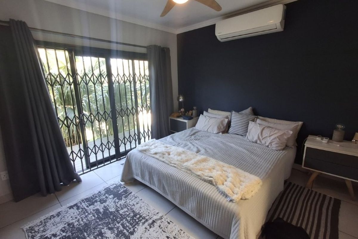 A well-maintained bedroom featuring tiled flooring, a ceiling fan, a split-system air conditioner, and sliding glass doors with security gates leading outdoors.