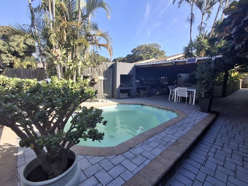 Outdoor entertainment area featuring a swimming pool, paved patio, and a covered built-in braai area, ideal for relaxed alfresco dining.