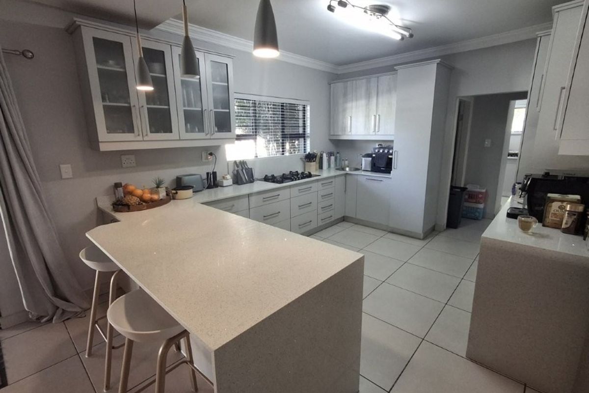 Modern kitchen featuring light-toned cabinetry, quartz countertops, a breakfast bar, gas hob, and tiled flooring with ample storage space.