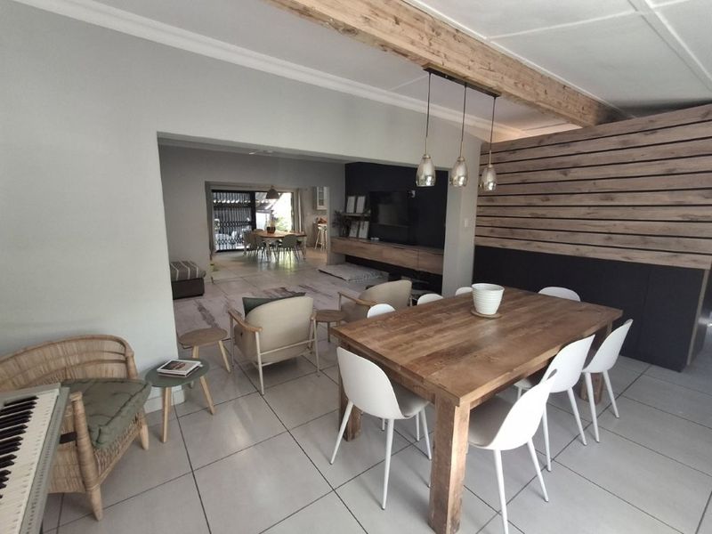Spacious open-plan living and dining area featuring tiled floors, a striking timber slat feature wall, exposed ceiling beams, and modern pendant lighting.