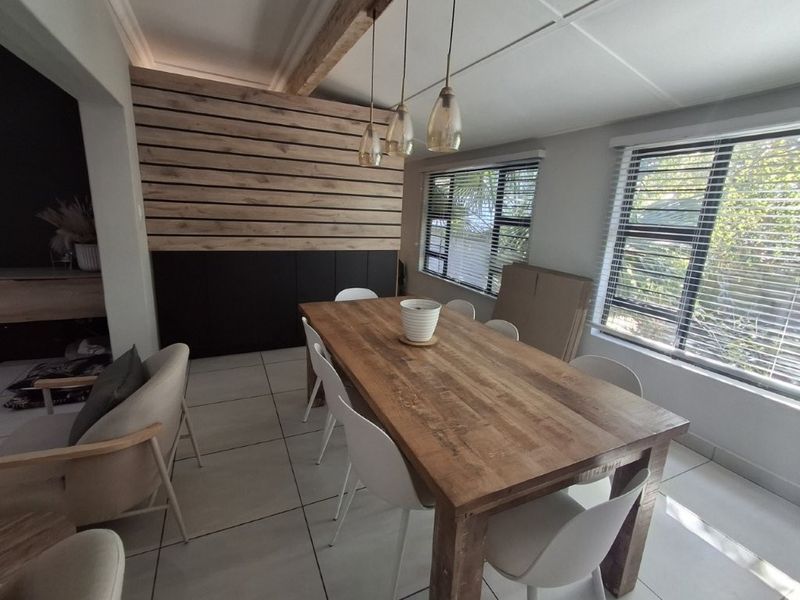 A modern dining area featuring a timber slat feature wall, built-in cabinetry, tiled flooring, and pendant lighting, with large windows providing natural light.