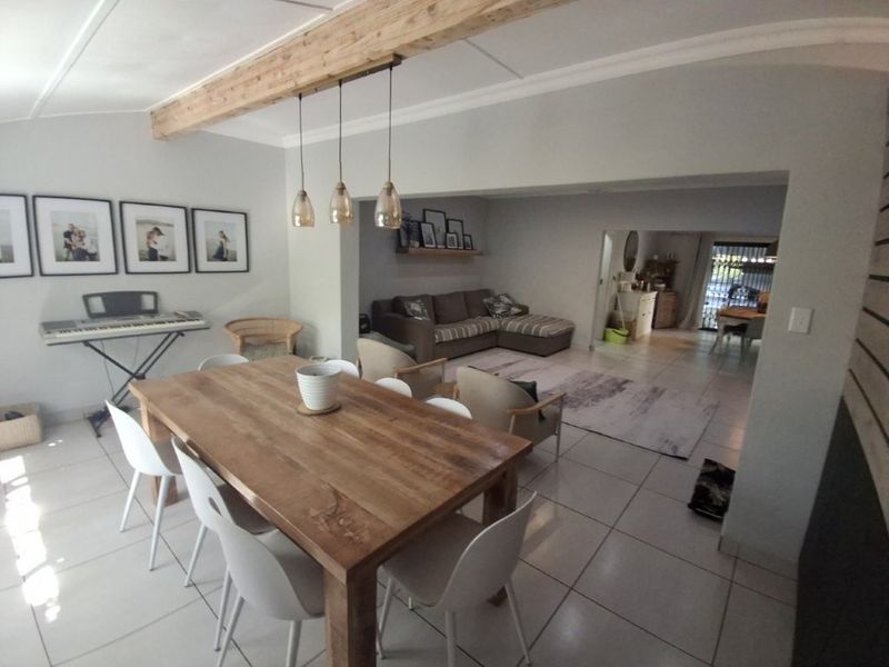 Spacious open-plan living and dining area featuring tiled flooring, an exposed timber ceiling beam, and neutral wall finishes.