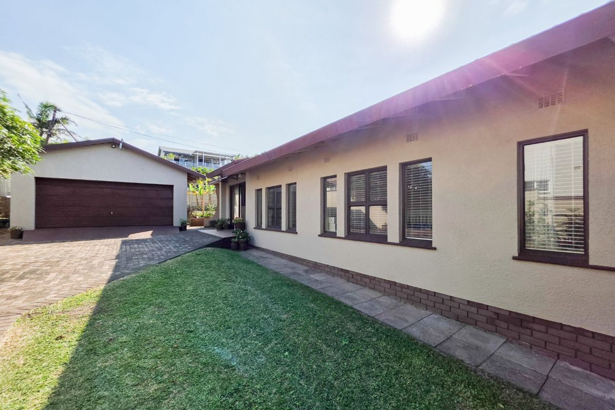 Rear view of the property featuring a paved driveway, detached garage, and a well-maintained lawn with a paved walkway along the building exterior.
