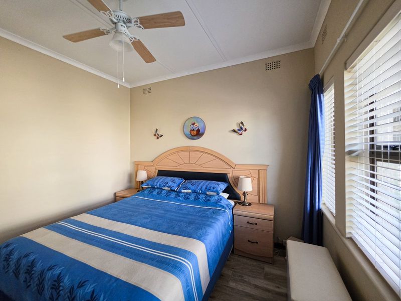 A well-maintained bedroom featuring a ceiling fan, neutral wall tones, and venetian blinds, offering a comfortable and functional living space.