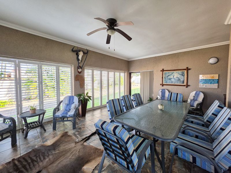 Spacious covered patio featuring tiled flooring, ceiling fan, and large sliding glass doors with shutters, providing seamless indoor-outdoor flow.