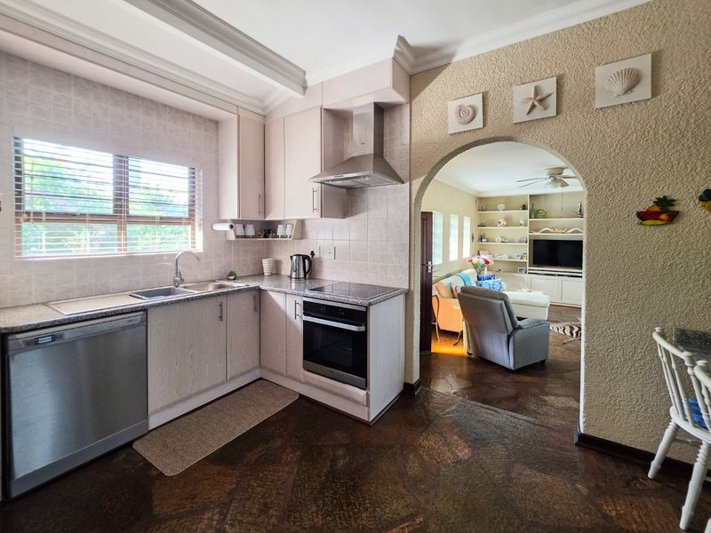 A functional kitchen featuring built-in cabinetry, granite countertops, and integrated appliances, connected to the living area through a classic arched doorway.
