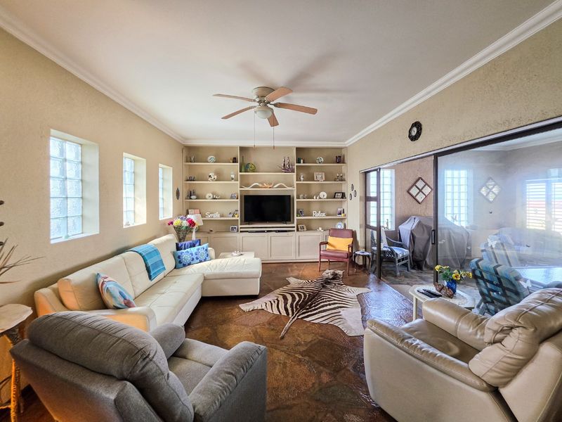 Spacious living room featuring a large built-in shelving unit, stone tile flooring, ceiling fan, and sliding glass doors leading to an enclosed patio area.
