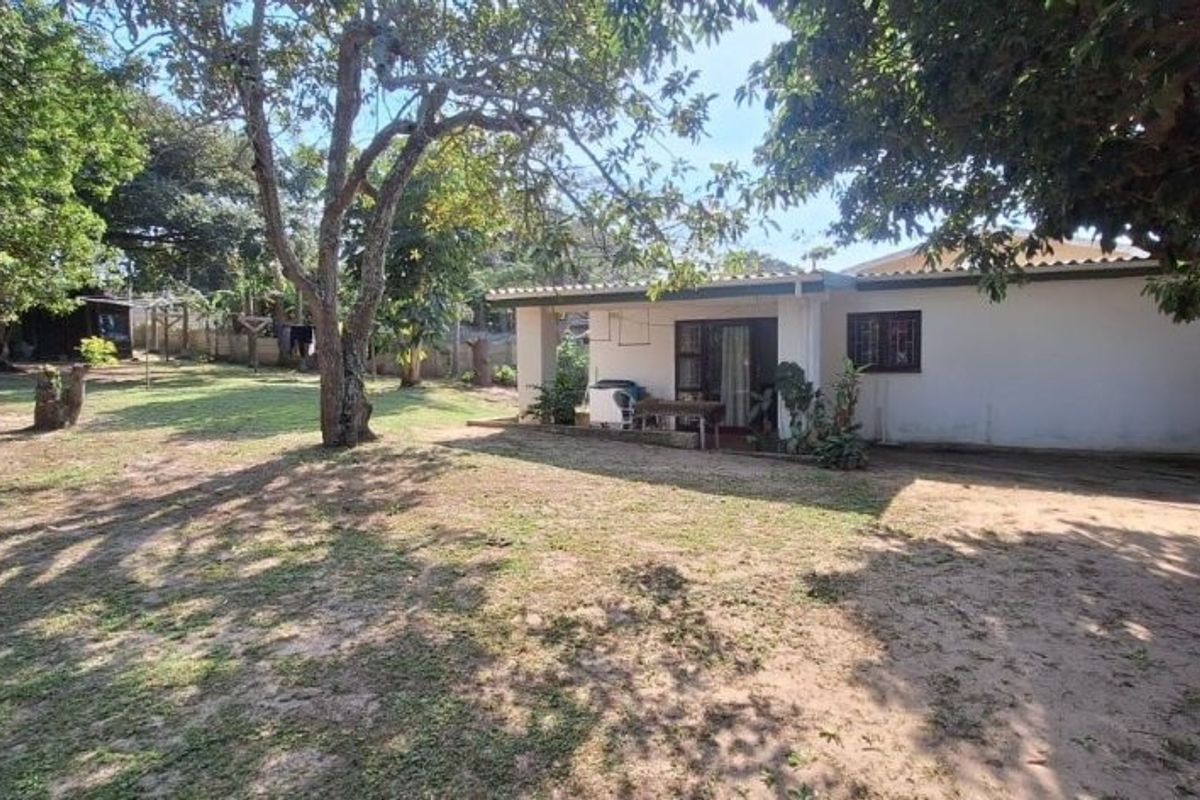 Rear view of the house featuring a covered patio, sliding glass doors with security bars, and a large, tree-shaded garden area.