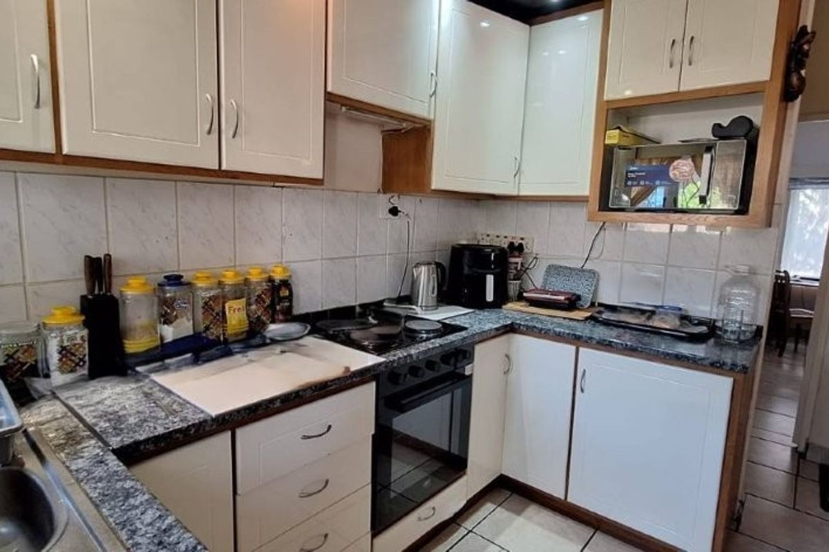 A functional kitchen featuring white cabinetry, granite-look laminate countertops, tiled backsplash, and integrated cooking appliances with tiled flooring.