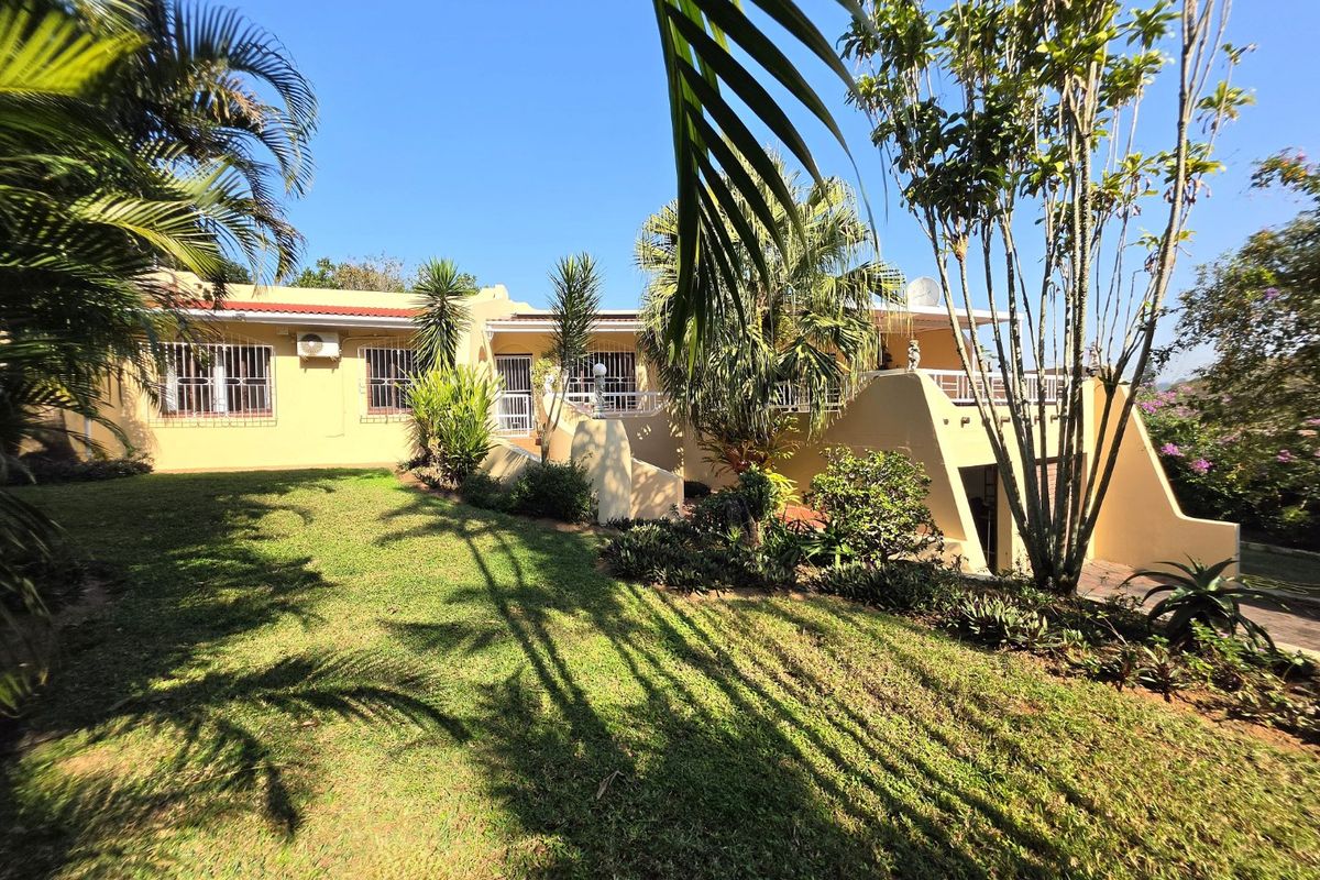 Rear view of the property featuring a landscaped garden, raised patio area, and exterior wall-mounted air conditioning unit.