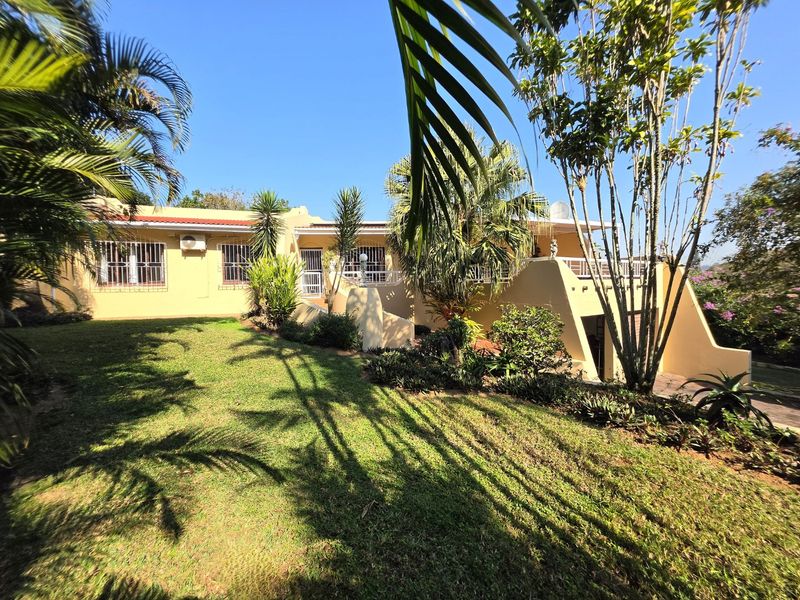 Rear view of the property featuring a landscaped garden, raised patio area, and exterior wall-mounted air conditioning unit.