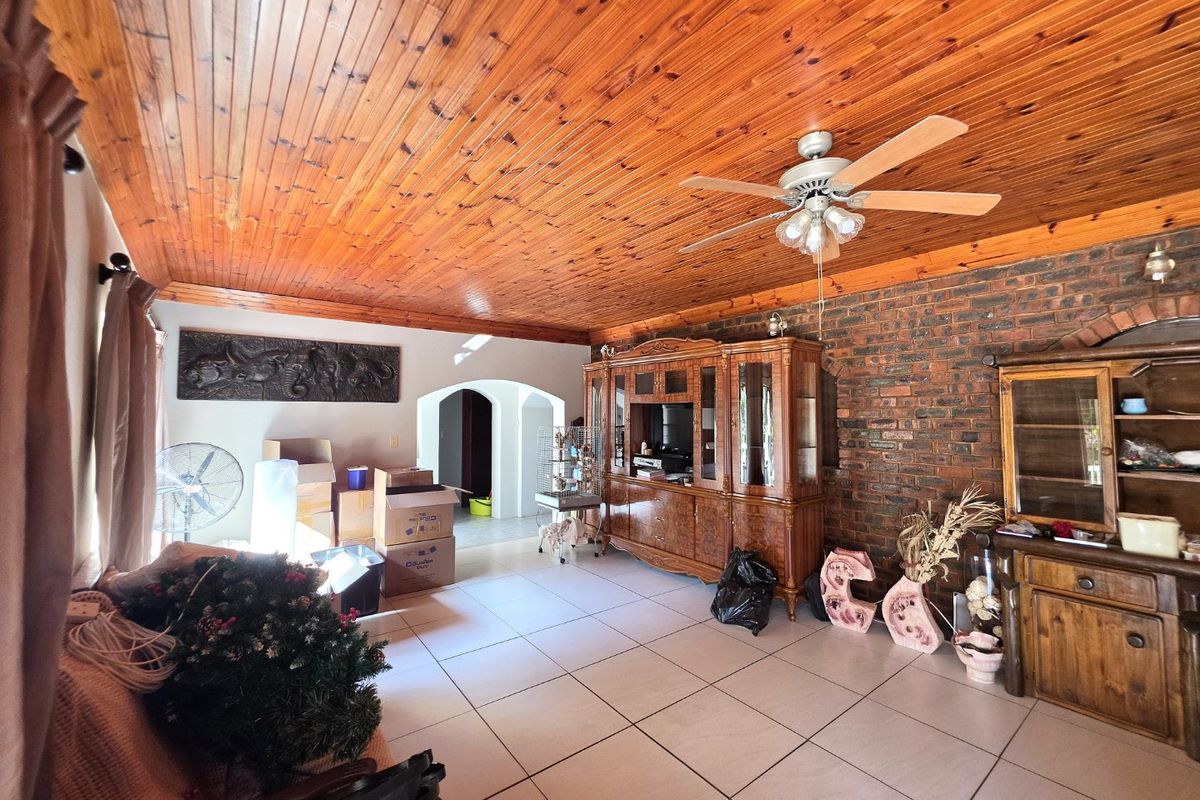 Spacious living room featuring a distinctive timber tongue and groove ceiling, exposed brick wall, and tiled flooring with an open archway leading to other areas.