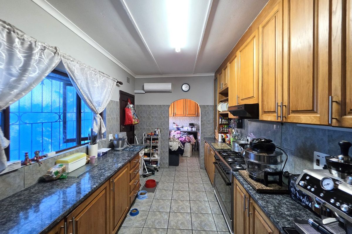 A functional galley-style kitchen featuring timber cabinetry, granite countertops, a gas hob with extractor, and tiled flooring, leading through an archway to an adjacent space.