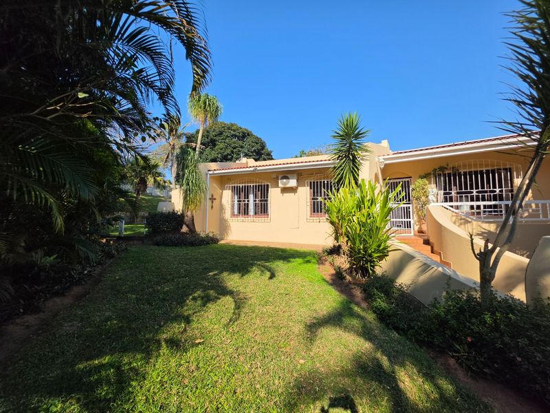 A well-maintained rear exterior view featuring a landscaped garden, a paved patio area, and secure window bars on the building facade.