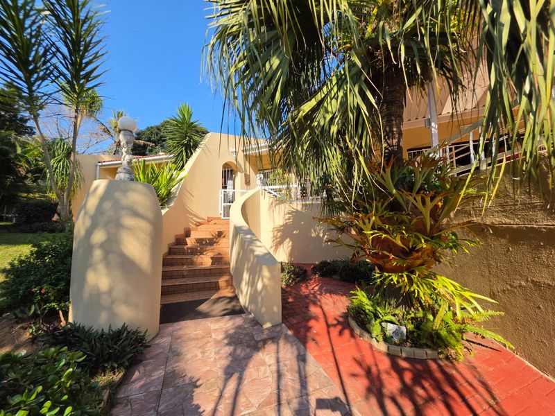 Front entrance featuring a curved masonry staircase with tiled steps, leading to a raised patio area surrounded by established garden landscaping.